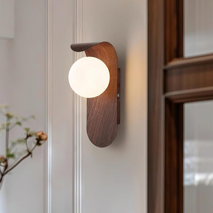 Nordisk vägglampa med träinspirerad stomme och rund glasglob för varm och mjuk belysning